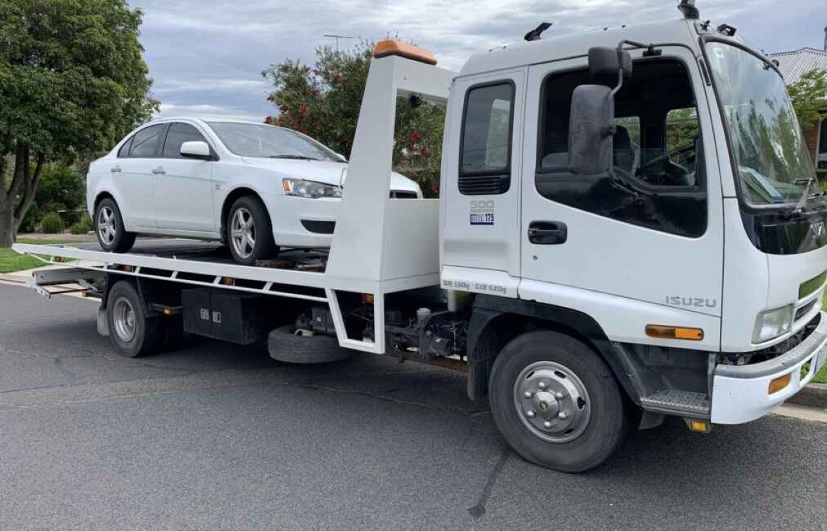 Emergency towing service with flatbed truck carrying white sedan in Lindenhurst, NY