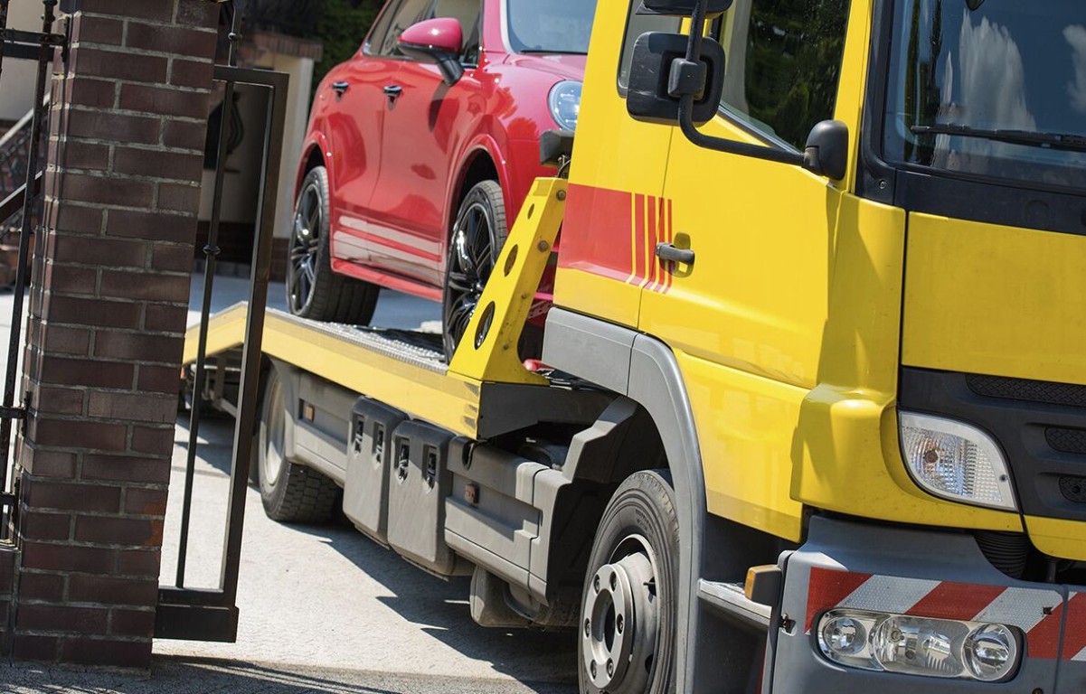 Yellow flatbed tow truck safely transporting red car through a neighborhood street in Lindenhurst, NY